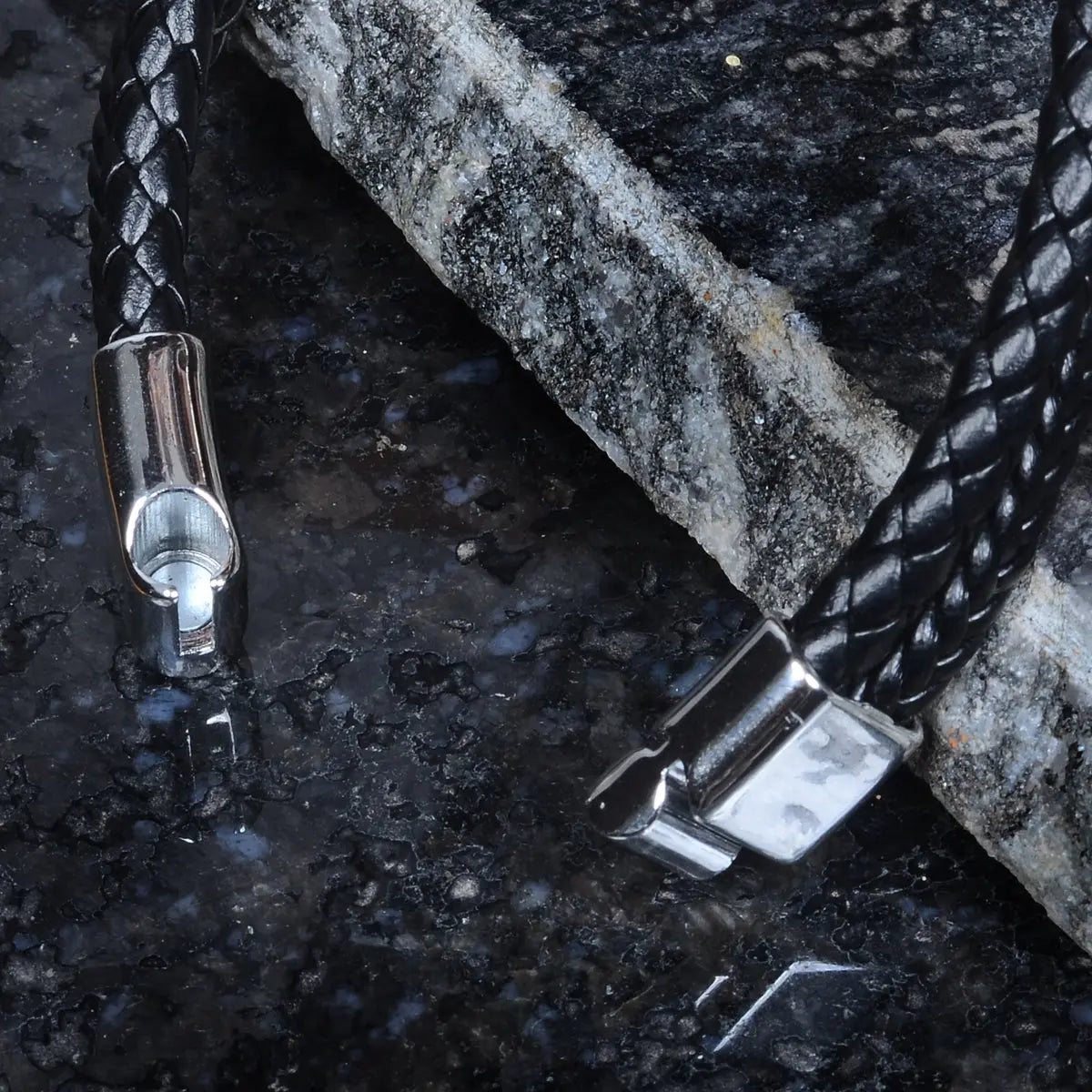 Black braided leather bracelet for men with silver clasp on a textured surface