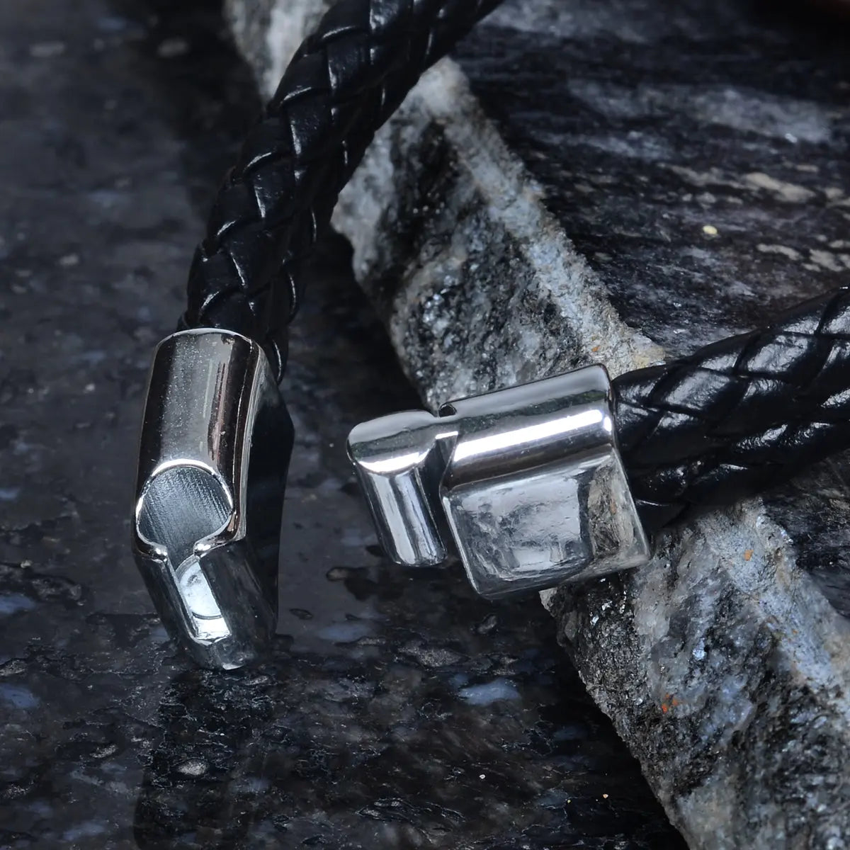 Black braided leather bracelet for men with silver clasp on stone surface by Supreme Stud