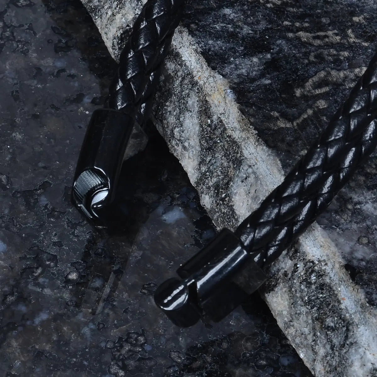 Black braided leather bracelet for men on a textured stone surface by Supreme Stud