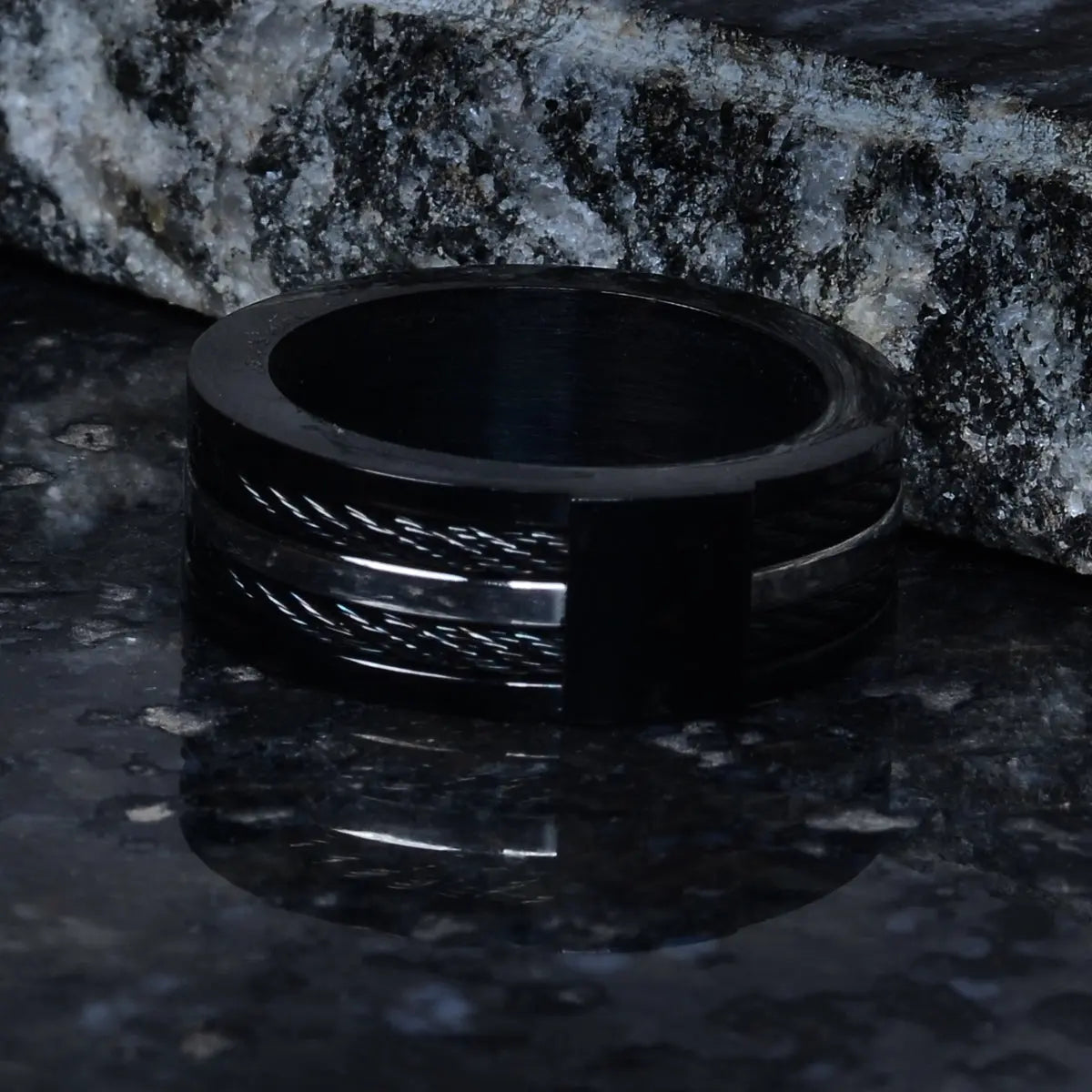Black steel ring for men on a dark stone surface by Supreme Stud