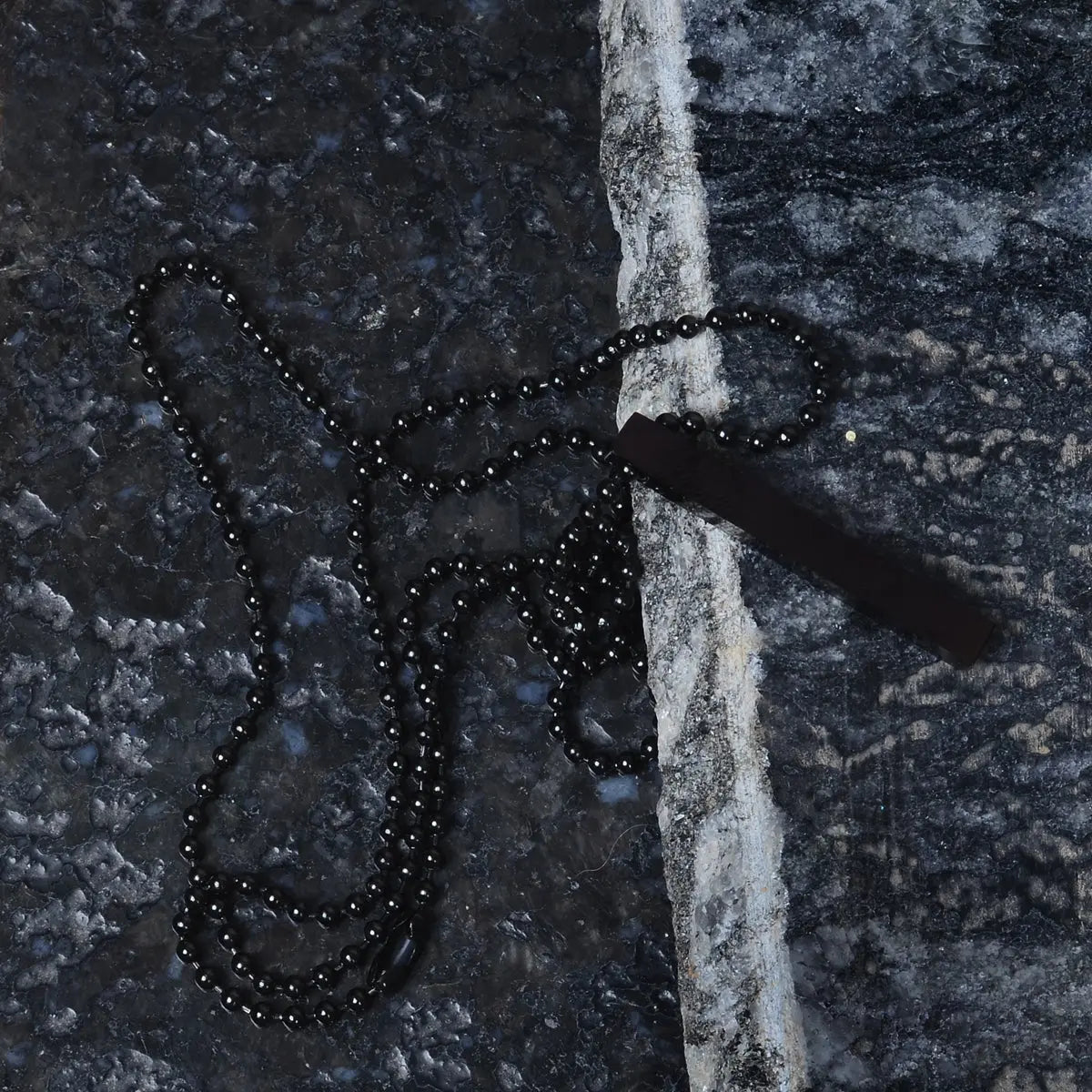 Black beaded steel pendant for men draped over a textured dark surface by Supreme Stud