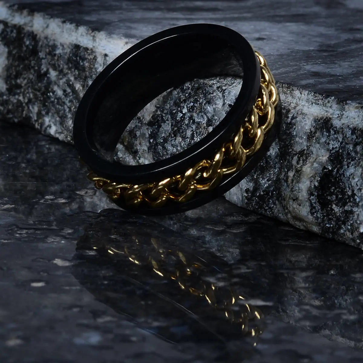 Black ring for men with gold chain design on a dark stone surface by Supreme Stud