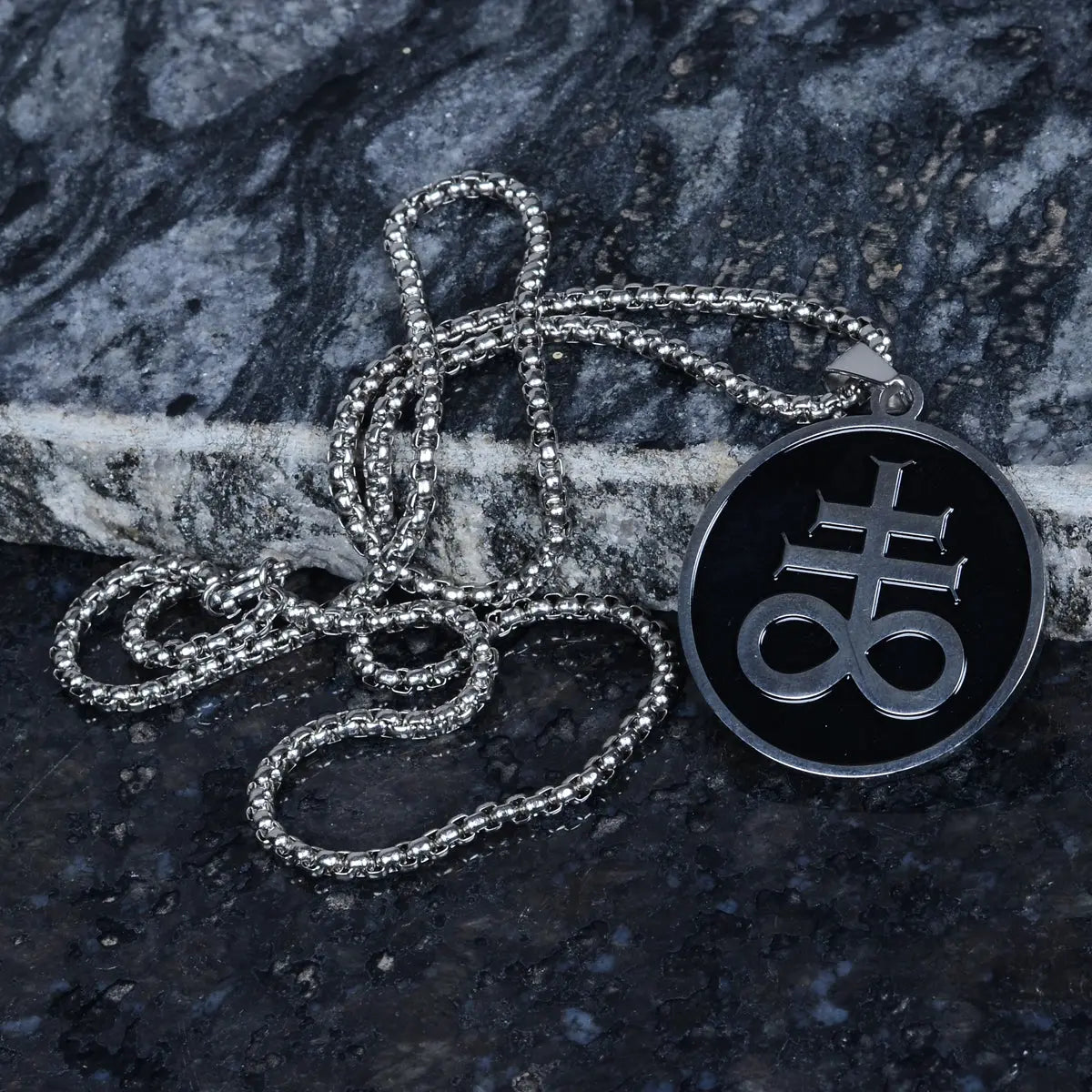Men's pendant with a black necklace featuring a symbol on a dark stone surface by Supreme Stud