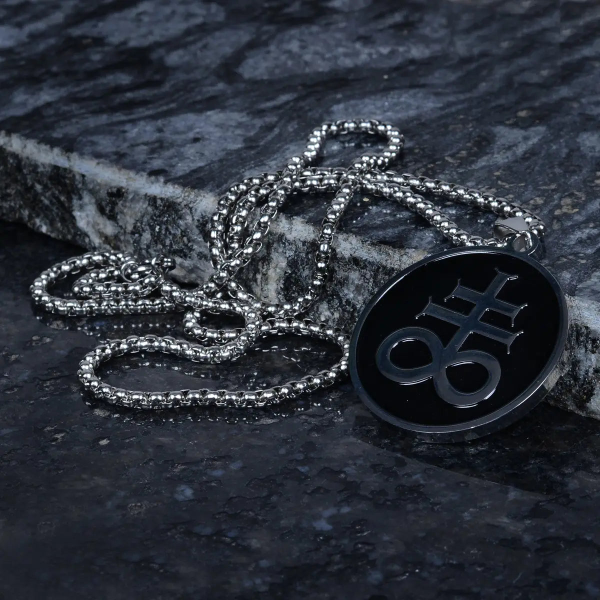 Necklace with a black pendant featuring a symbol on a dark stone surface by Supreme Stud