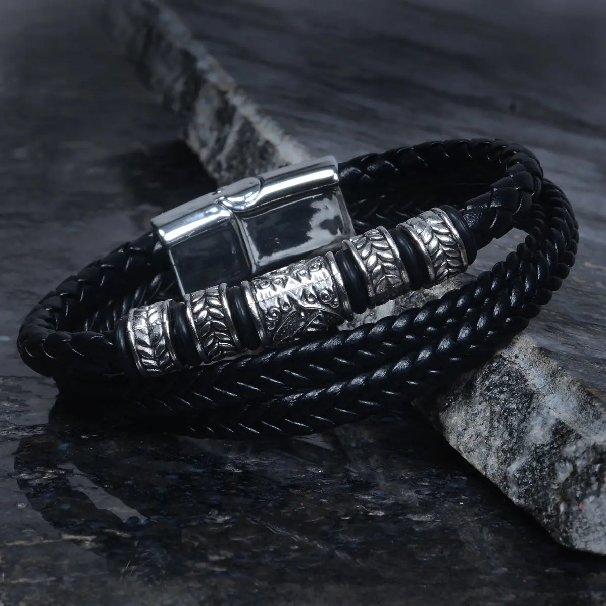Black braided leather bracelet for men with silver metal accents on a dark stone surface by Supreme Stud
