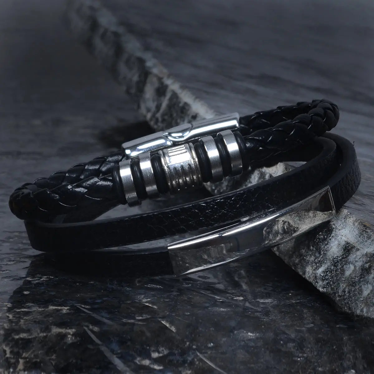 Black braided leather bracelet for men with metal clasp on a dark stone surface by Supreme Stud