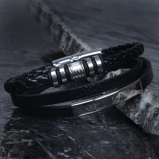 Black braided leather bracelet for men with metal clasp on a dark stone surface by Supreme Stud