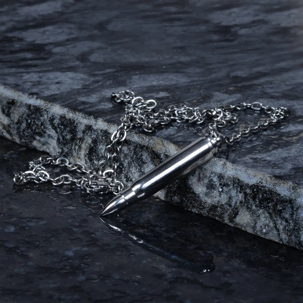Steel necklace for men with a bullet-shaped pendant on a dark stone surface by Supreme Stud