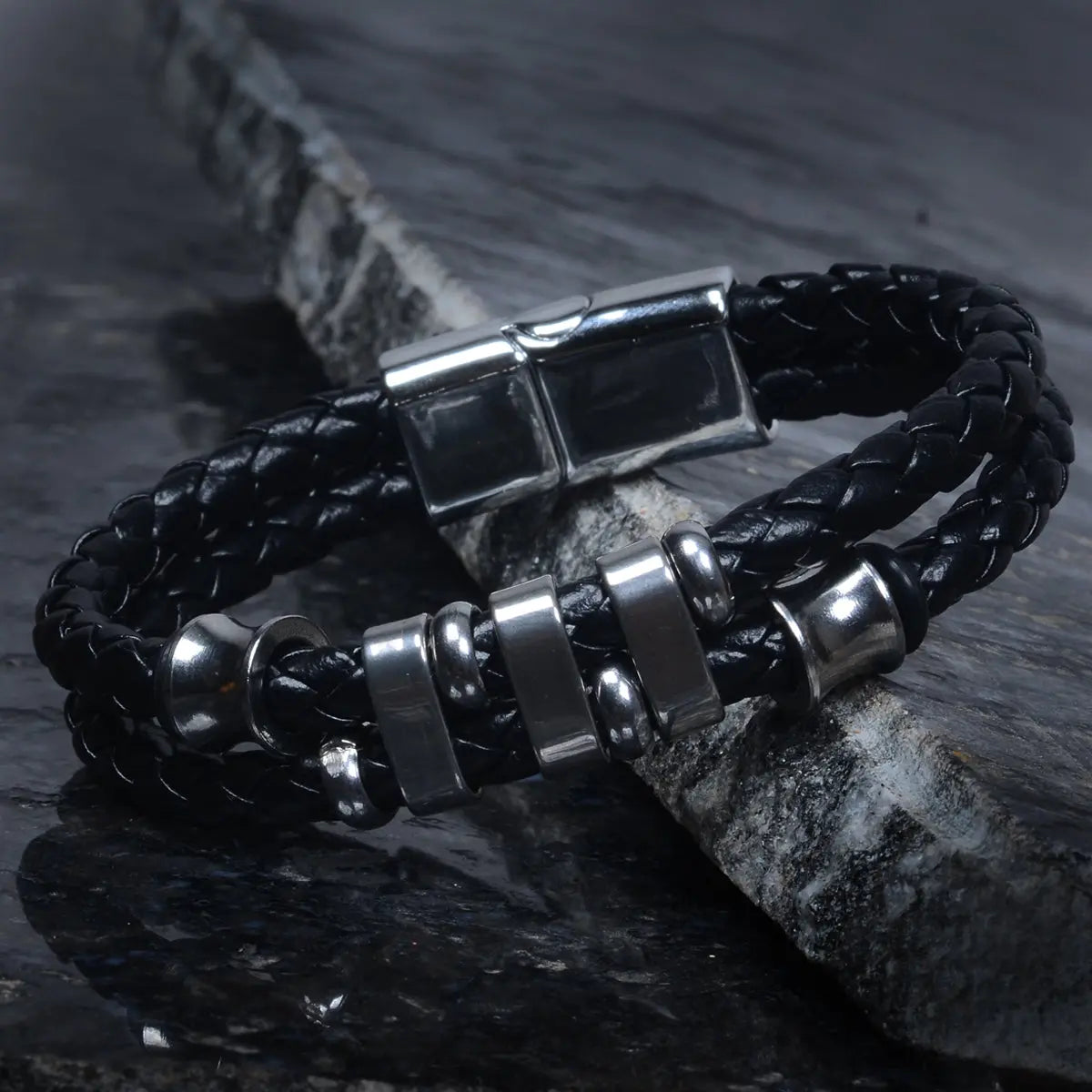Black braided leather bracelet for men with silver metal beads on a dark stone surface by Supreme Stud